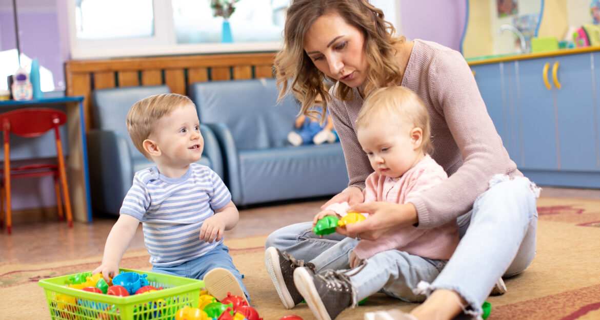 Assistante maternelle jouant avec deux jeunes enfants dans un espace d'accueil, accompagnement des familles dans le cadre du mode de garde individuel.