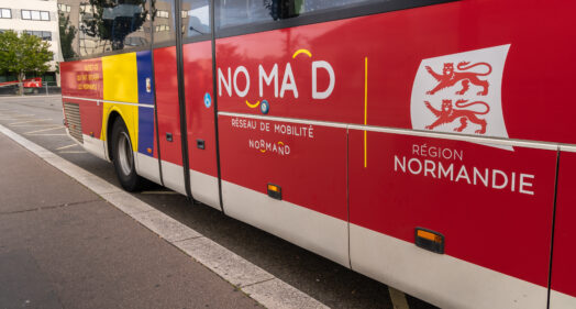 Autocar rouge du réseau de mobilité Nomad en Normandie, stationné sur la voie publique