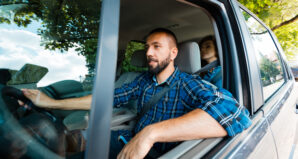 Un homme souriant conduit une voiture avec une passagère assise à l'arrière.