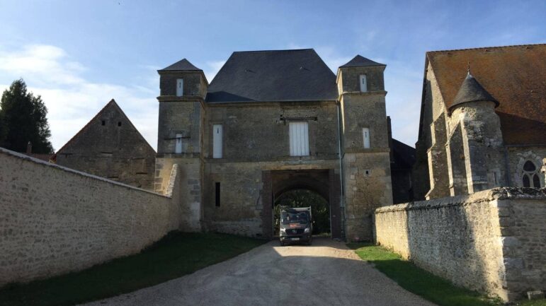 Camion de l'entreprise BM Couverture passant sous le porche d'un édifice historique en pierre