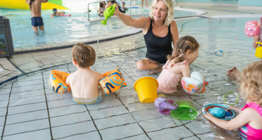 Des enfants de la crèche sont dans un bassin de la piscine avec une accompagnante, qui joue avec l'un d'eux.