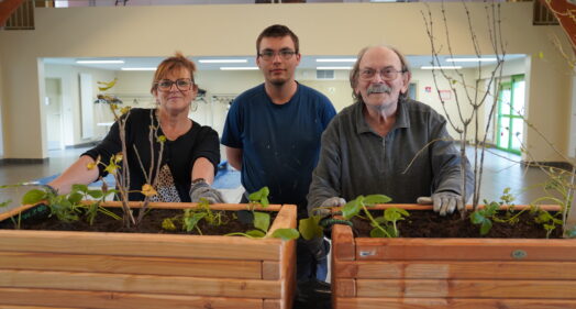 Un jeune, une encadrante et un résident de l'Ehpad de Fleury-sur-Andelle posent devant des jardinières toutes neuves.